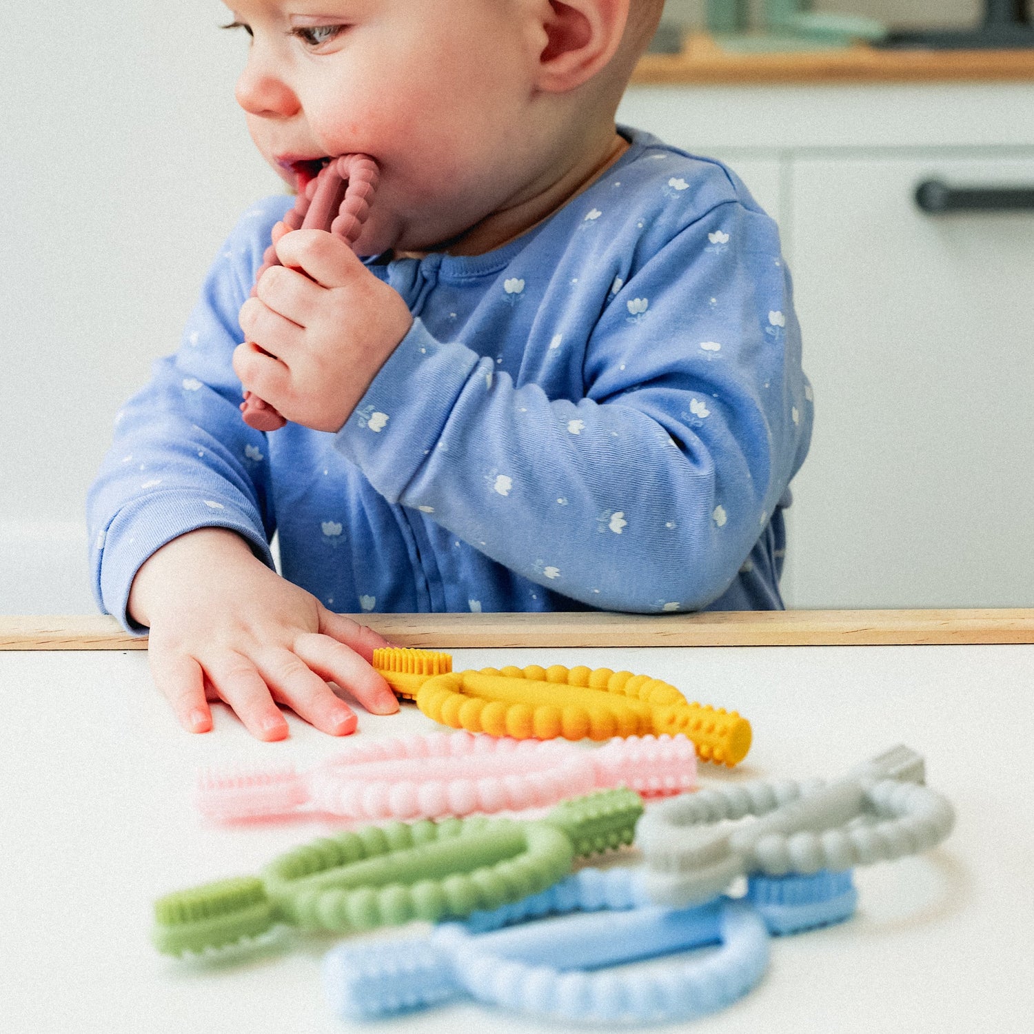 Baby playing with colorful teethers on a kitchen counter.