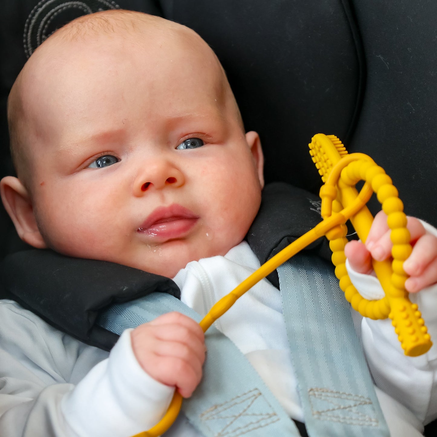 Baby in a car seat holding a yellow teething toy