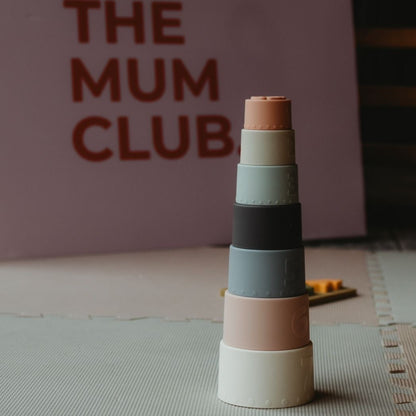 Stack of colorful cylindrical blocks on a mat with 'The Mum Club' sign in the background