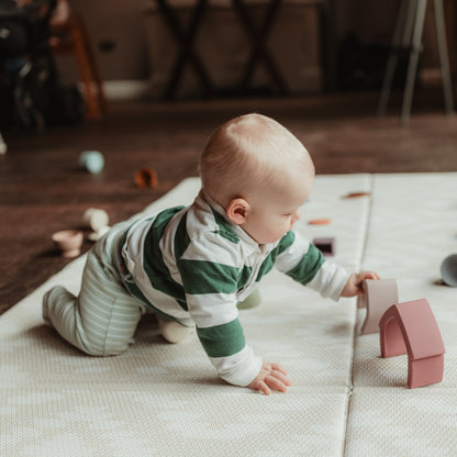 Baby in a striped onesie playing with toys on a mat indoors.