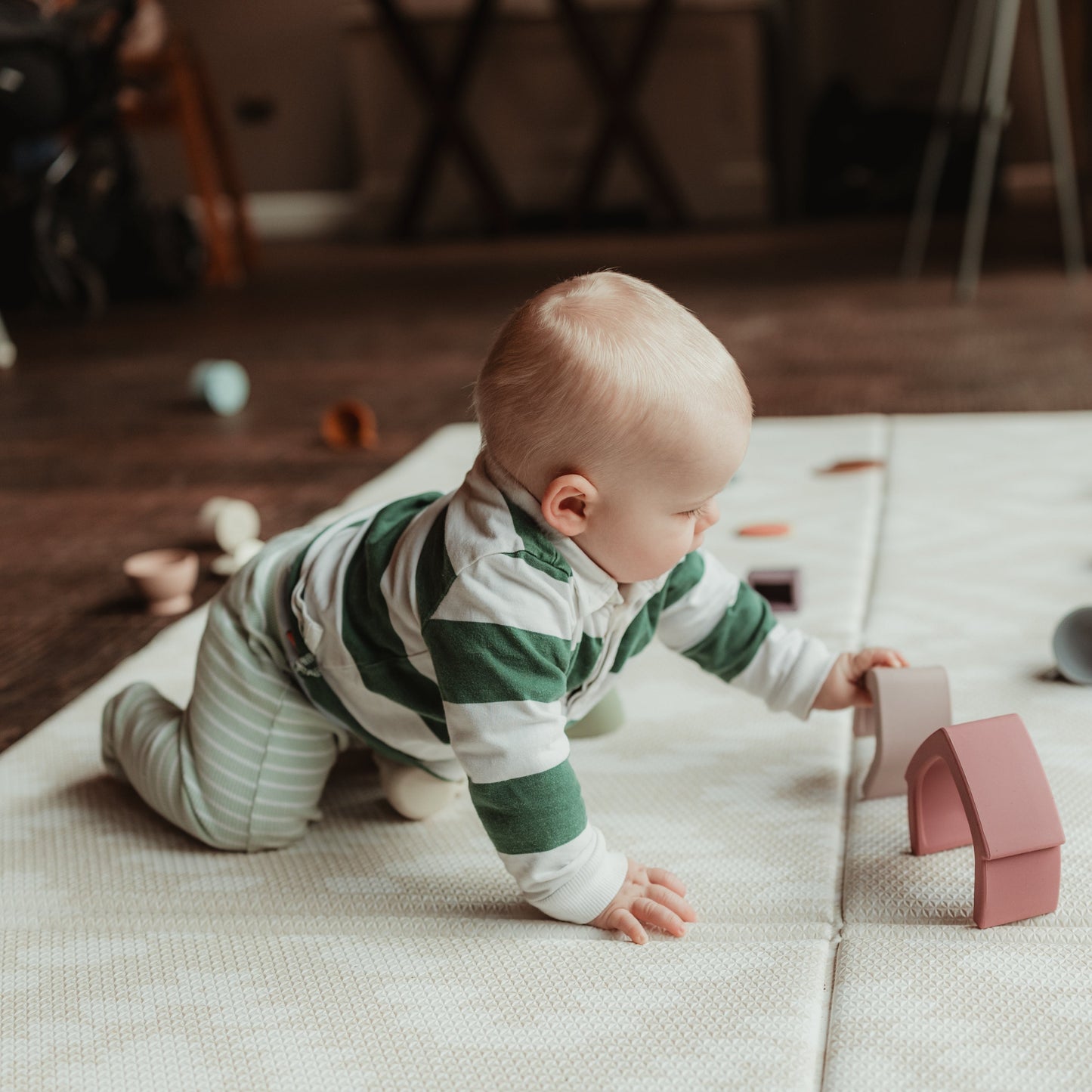 Baby crawling towards silicone stacking house toys on a soft play mat
